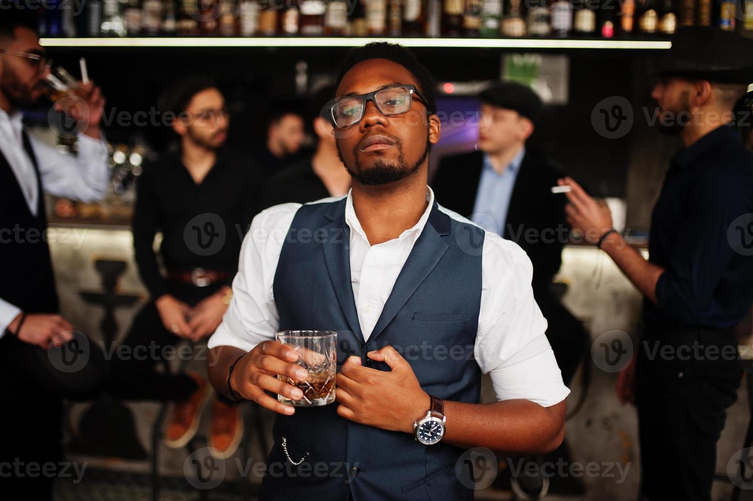 elegante hombre afroamericano contra un grupo de guapos gángsters retro bien vestidos pasan tiempo en el club, bebiendo en el mostrador del bar. despedida de soltero multiétnico de la mafia en el restaurante. foto