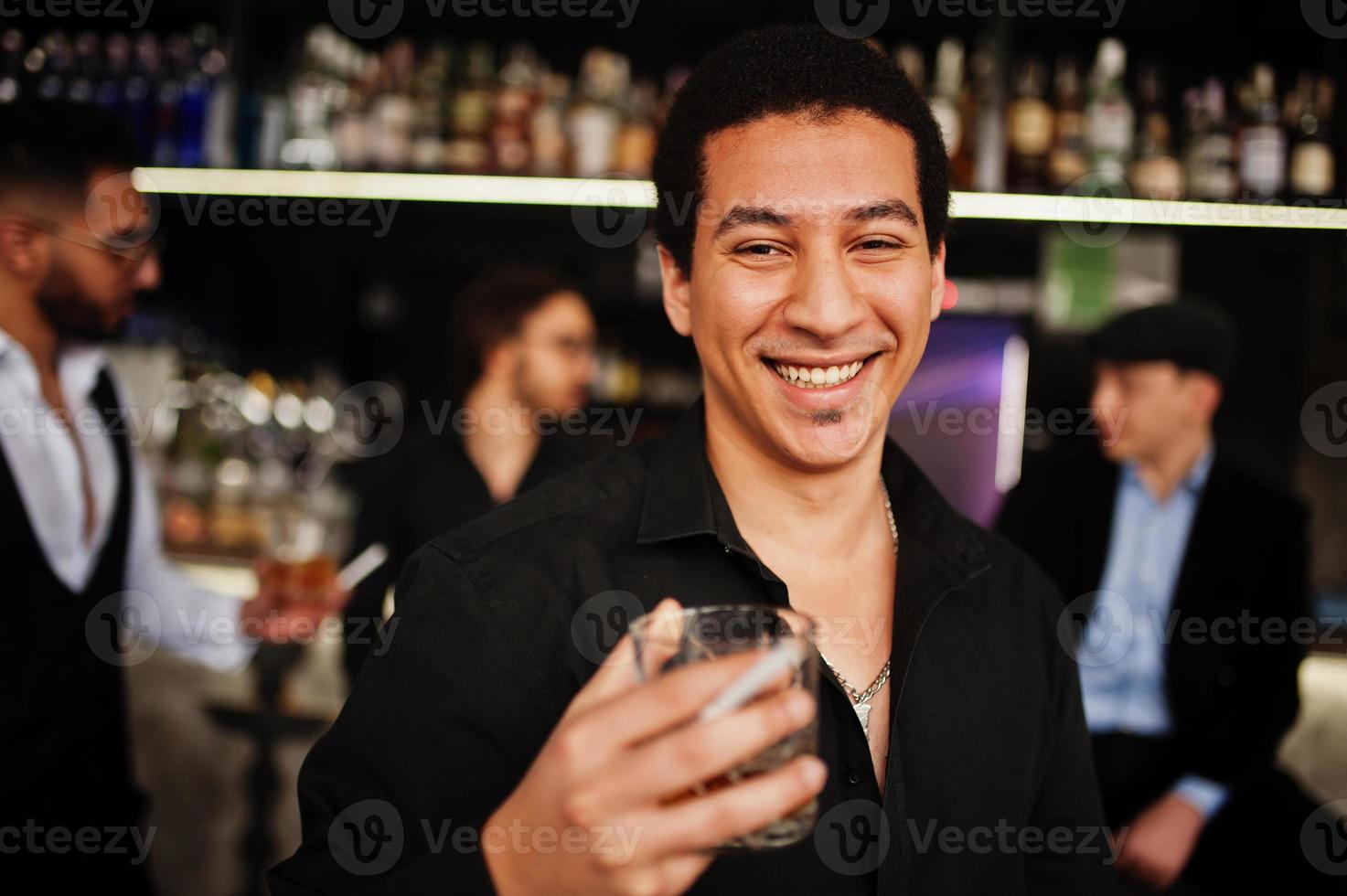 Stylish arab man against group of handsome retro well-dressed guys gangsters spend time at club, drinking on bar counter. Multiethnic male bachelor mafia party in restaurant. photo