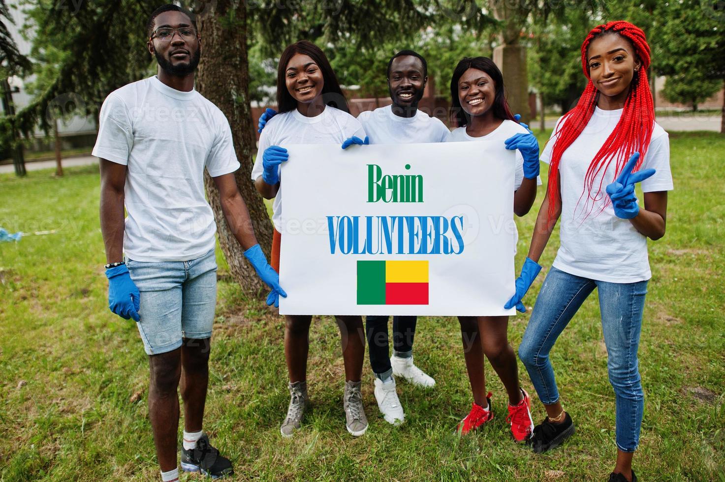 Group of happy african volunteers hold blank with Benin flag in park. Africa countries volunteering, charity, people and ecology concept. photo