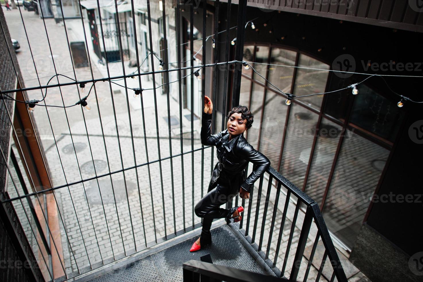 Fashionable beautiful african american woman posing in black leather jacket and pants at street. photo