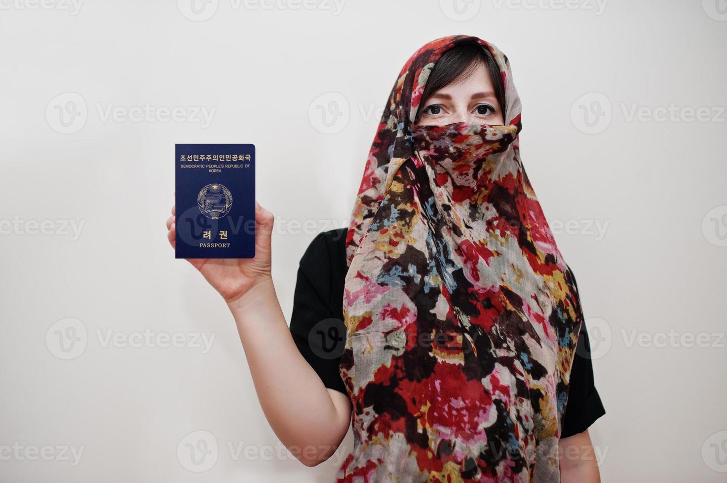 Young arabian muslim woman in hijab clothes hold Democratic People's Republic of Korea passport on white wall background, studio portrait. photo