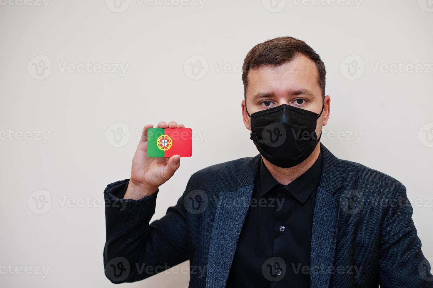 European man wear black formal and protect face mask, hold Portugal flag card isolated on white background. Europe coronavirus Covid country concept. photo