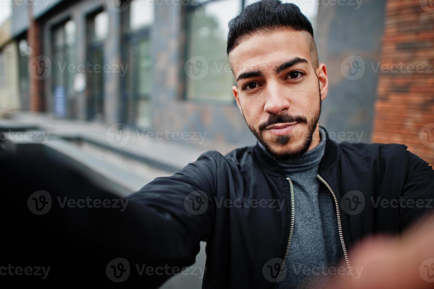 Portrait of stylish arab beard man wear grey turtleneck and black jaket. Arabian model guy make selfie by camera. photo