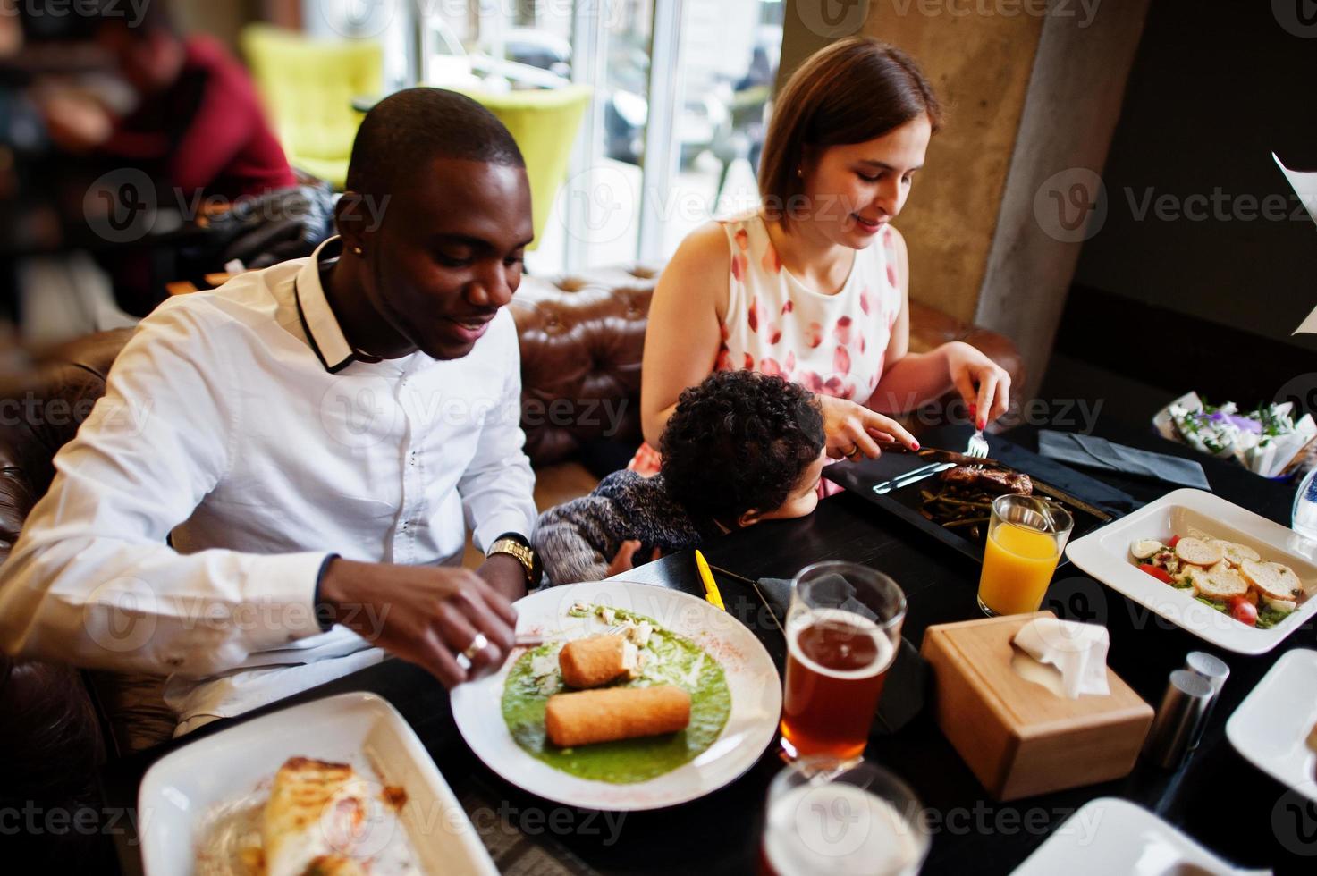 feliz familia multiétnica con niño chico pasar tiempo en el restaurante. relaciones de hombre africano y mujer europea blanca. foto