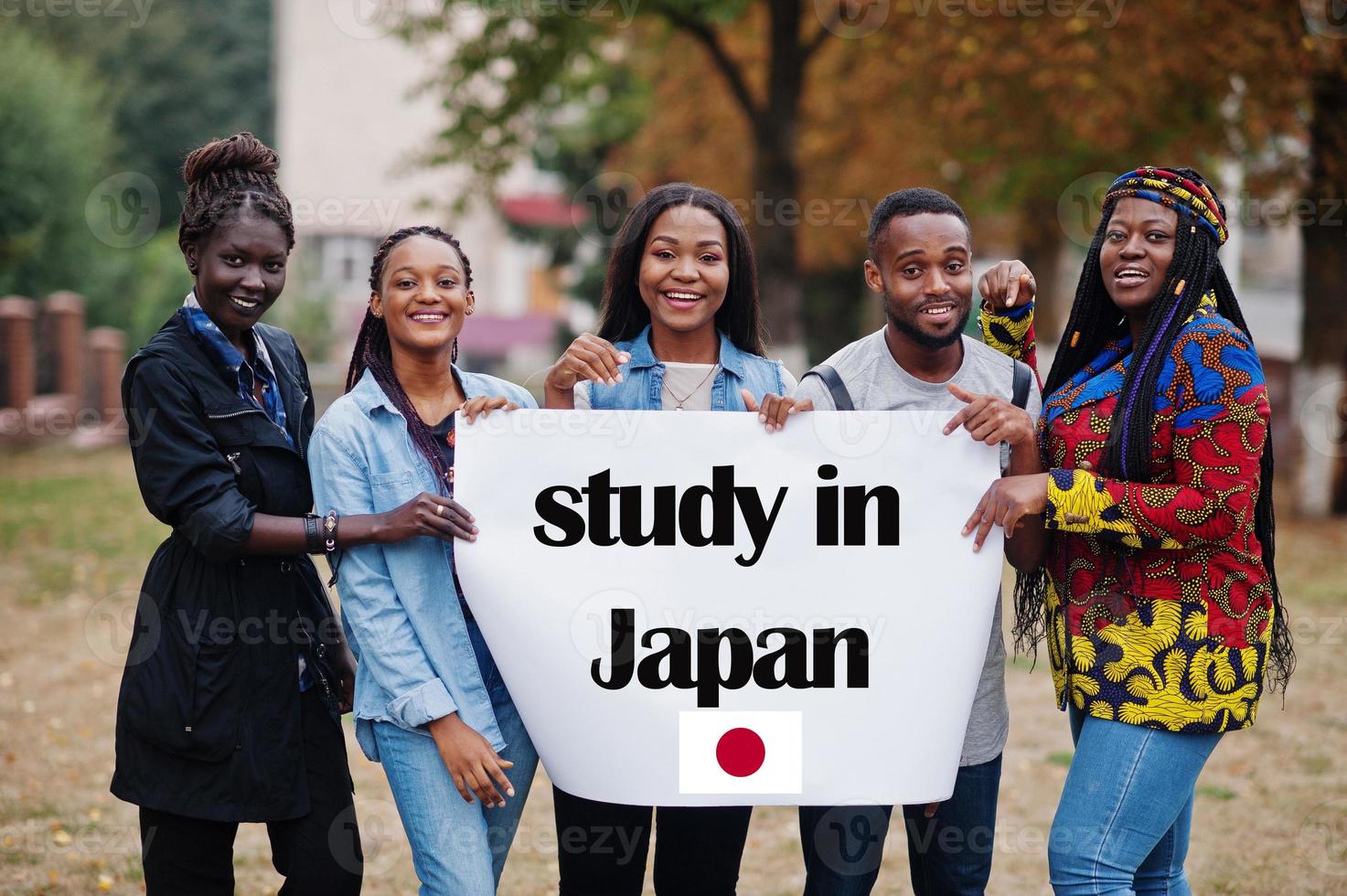 Study in Japan. Group of five african college students on campus at university yard hold white blank. Abroad countries for student concept. photo