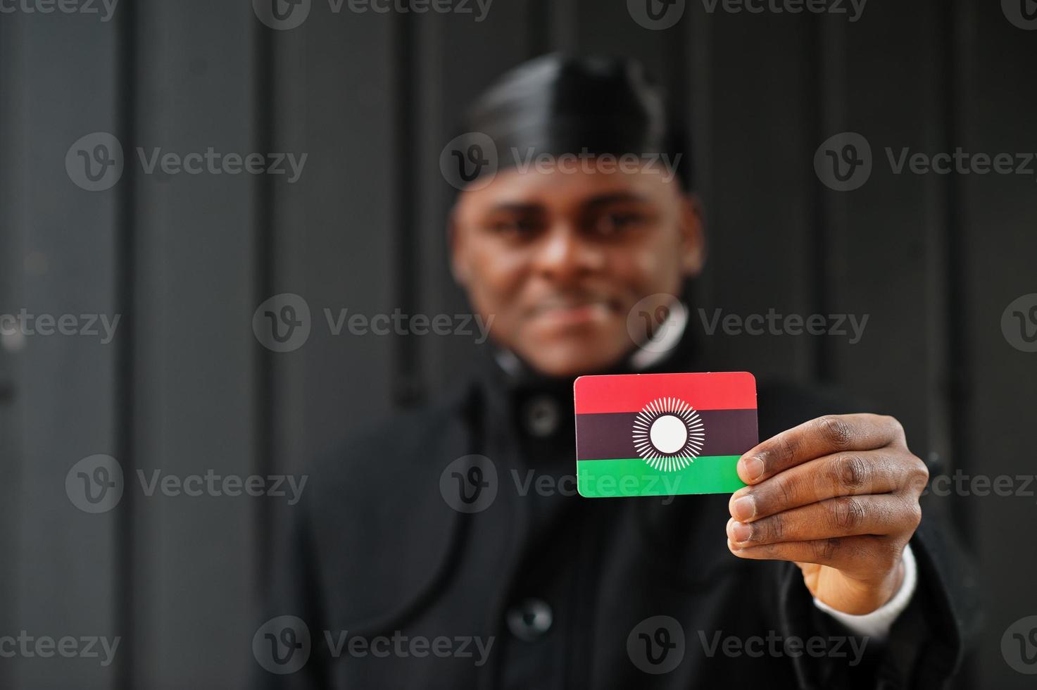 hombre africano usa durag negro sostiene la bandera de malawi a mano aislado fondo oscuro. foto