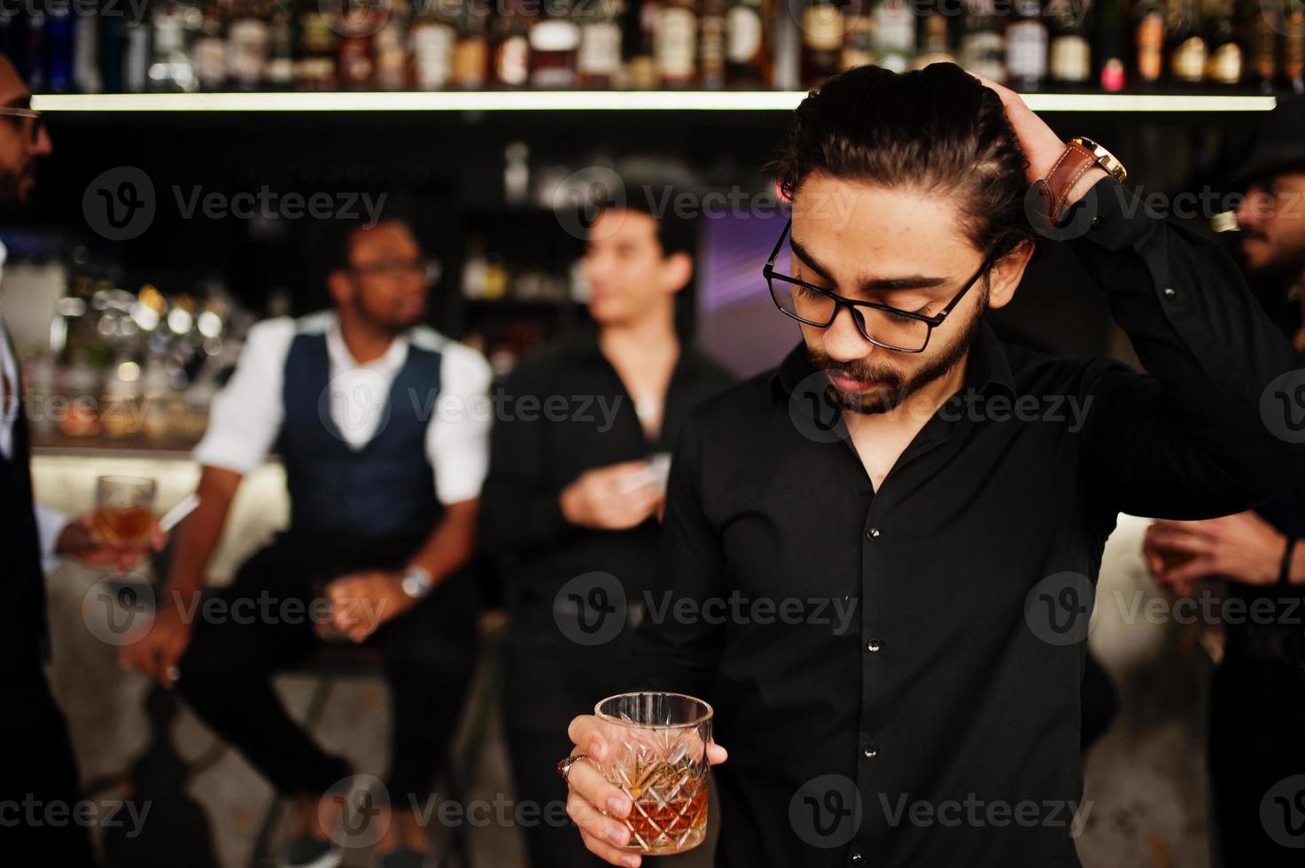 Stylish arab man against group of handsome retro well-dressed guys gangsters spend time at club, drinking on bar counter. Multiethnic male bachelor mafia party in restaurant. photo