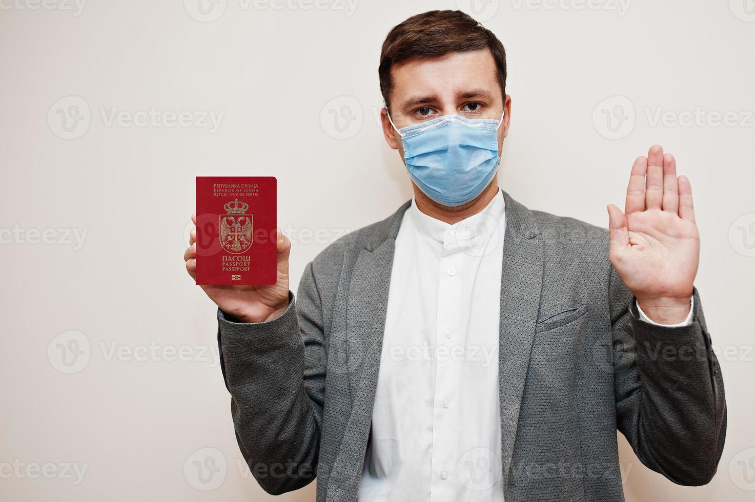 hombre europeo con ropa formal y máscara facial, muestre el pasaporte serbio con la mano de la señal de stop. bloqueo de coronavirus en el concepto de país de europa. foto