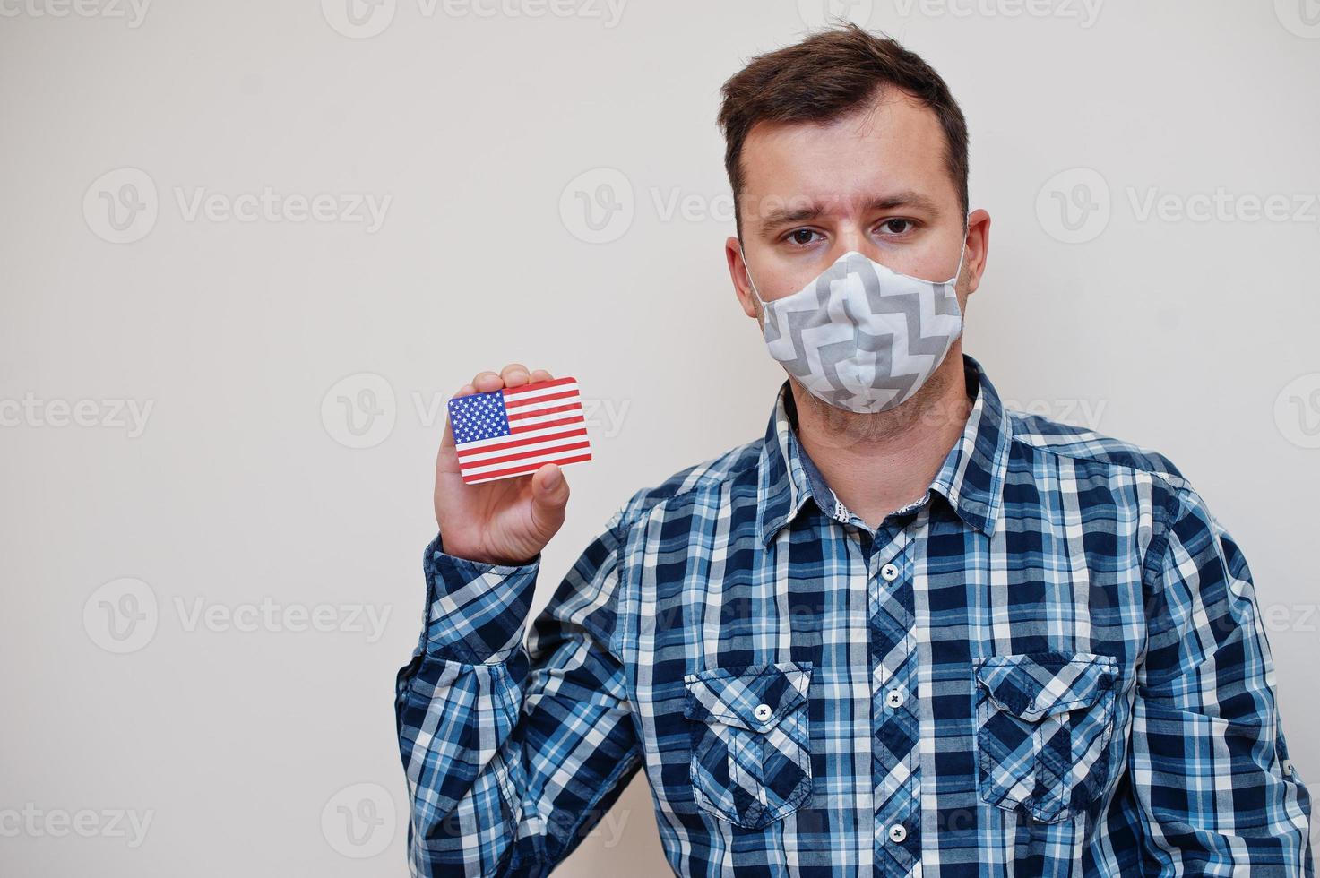 Man in checkered shirt show USA flag card in hand, wear protect mask isolated on white background. American countries Coronavirus concept. photo