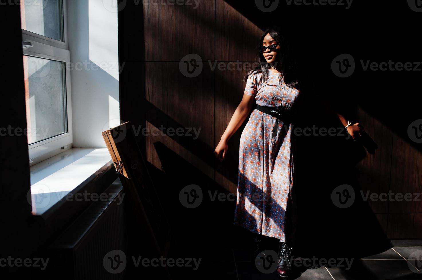 Game with shadows. Fashion portrait of african american woman in long dress and eyeglasses indoor. photo