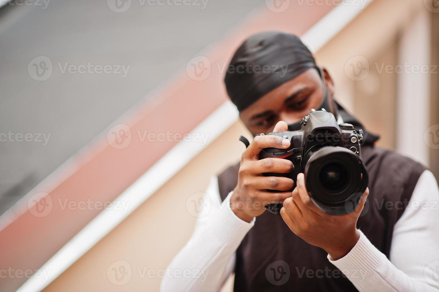 Young professional african american videographer holding professional camera with pro equipment. Afro cameraman wearing black duraq and face protect mask, making a videos. photo