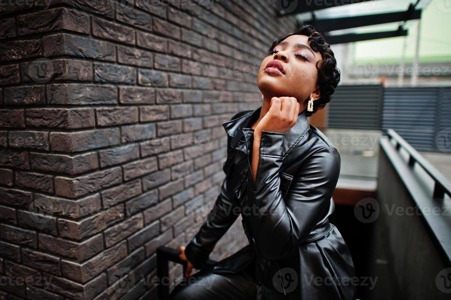 moda hermosa mujer afroamericana posando en chaqueta de cuero negro en la calle. pendiente en la nariz. foto