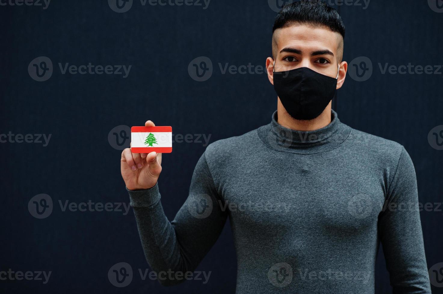 Middle eastern man in gray turtleneck and black face protect mask show Lebanon flag isolated background. photo