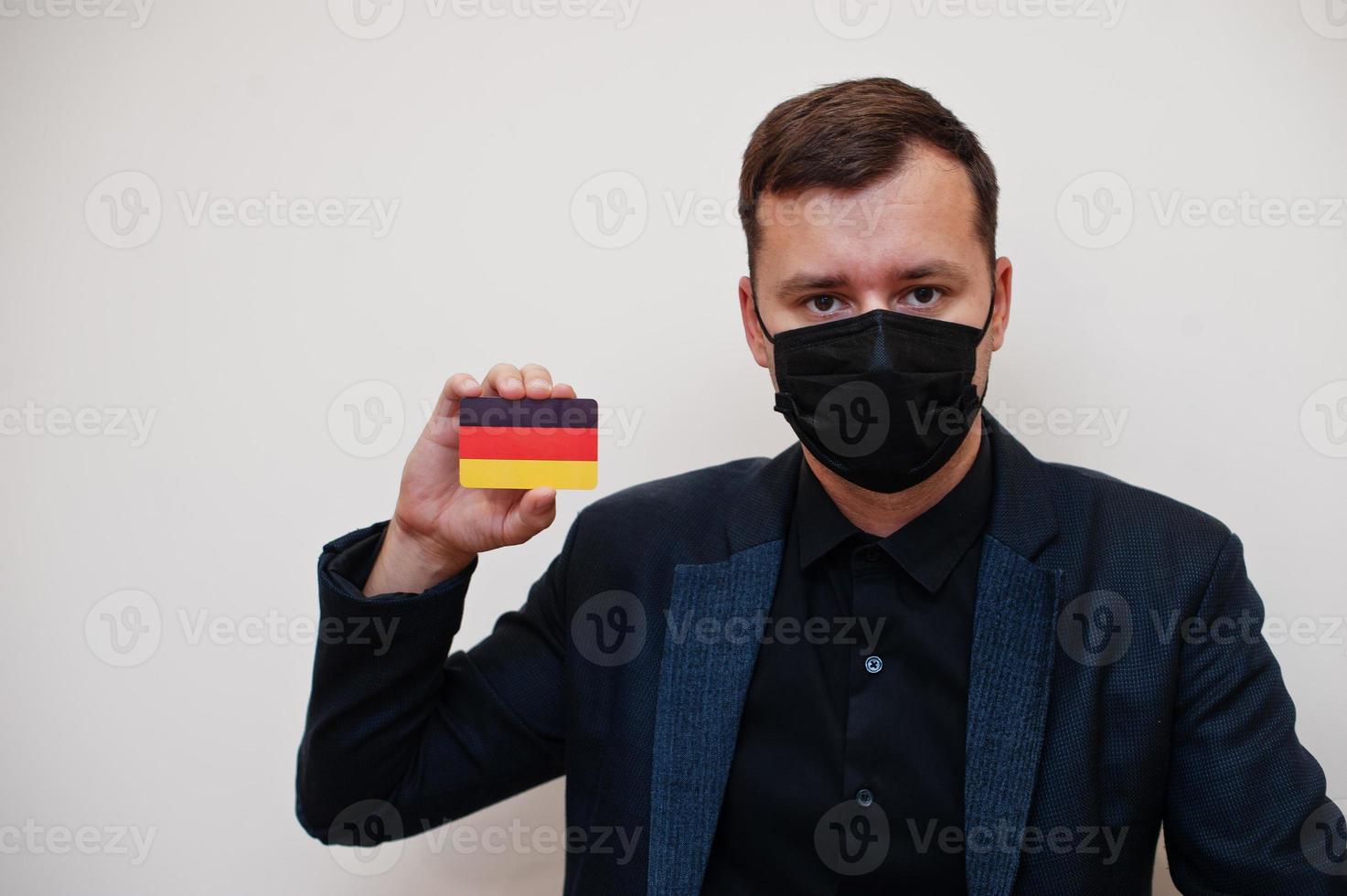 European man wear black formal and protect face mask, hold Germany flag card isolated on white background. Europe coronavirus Covid country concept. photo