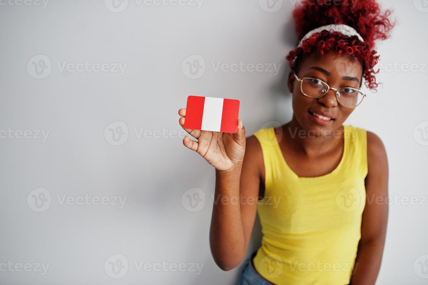 mujer afroamericana con cabello afro, use camiseta amarilla y anteojos, sostenga la bandera de perú aislada sobre fondo blanco. foto