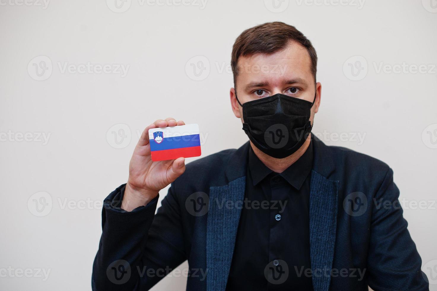 European man wear black formal and protect face mask, hold Slovenia flag card isolated on white background. Europe coronavirus Covid country concept. photo