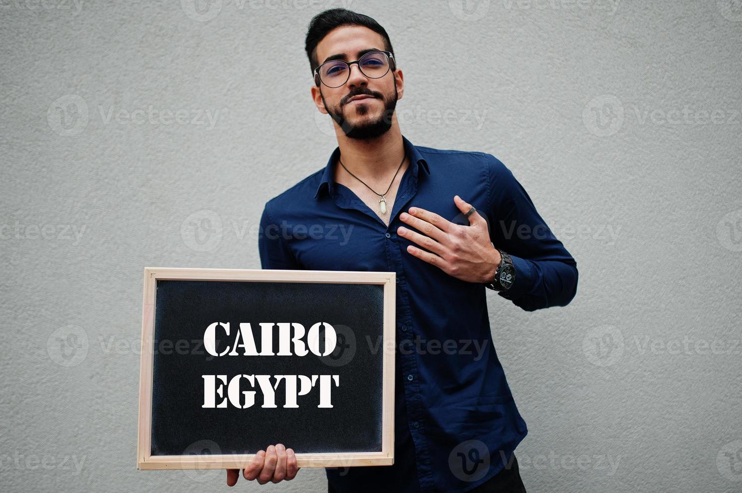 el hombre árabe usa camisa azul y anteojos sostiene una tabla con la inscripción en el cairo, egipto. ciudades más grandes en el concepto del mundo islámico. foto