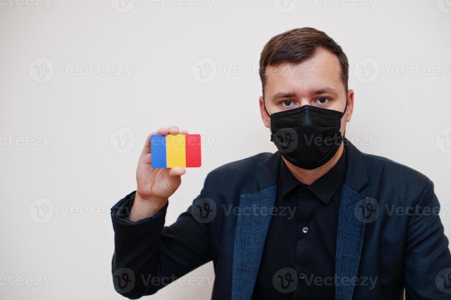 European man wear black formal and protect face mask, hold Romania flag card isolated on white background. Europe coronavirus Covid country concept. photo