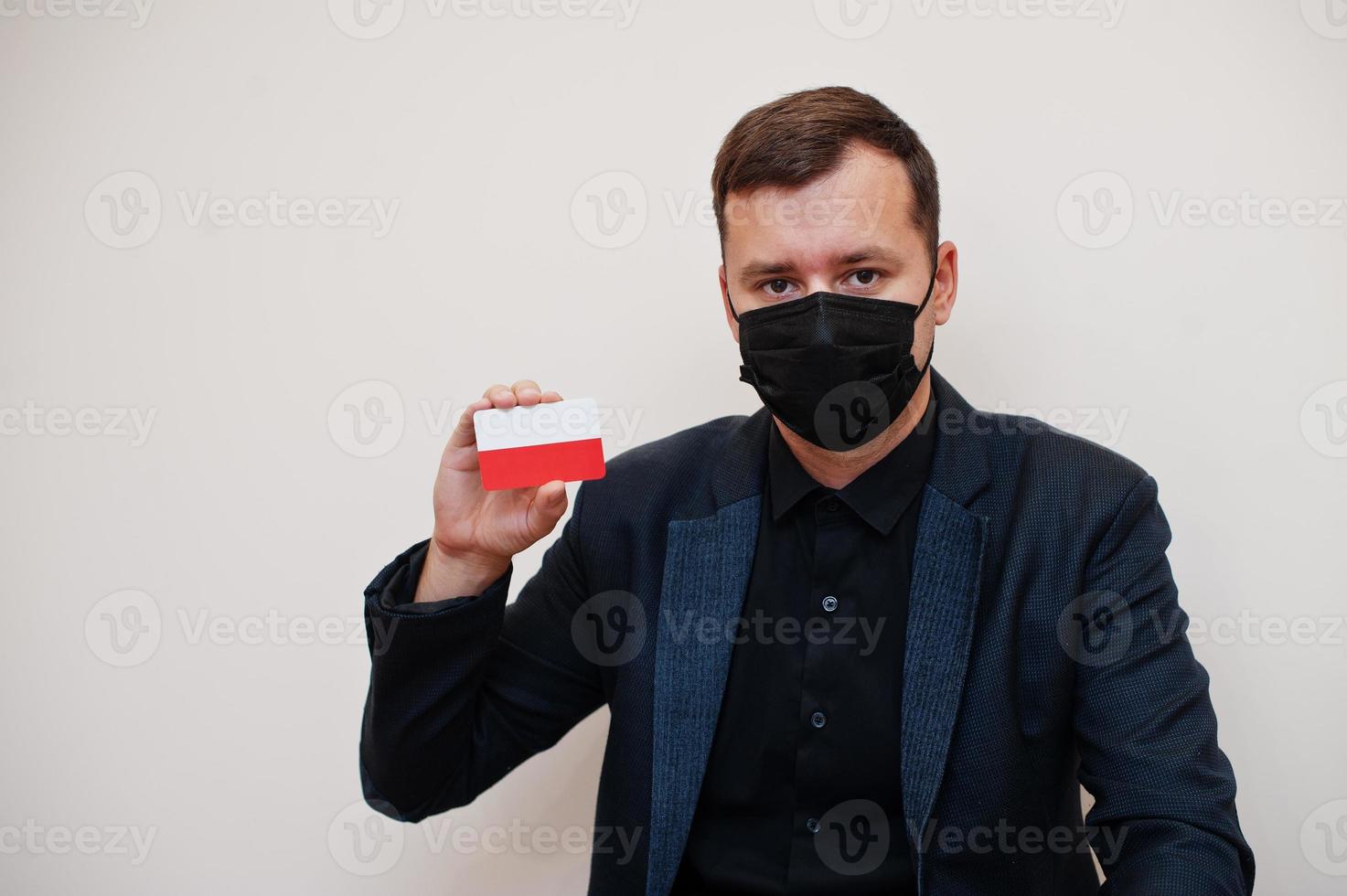 European man wear black formal and protect face mask, hold Poland flag card isolated on white background. Europe coronavirus Covid country concept. photo