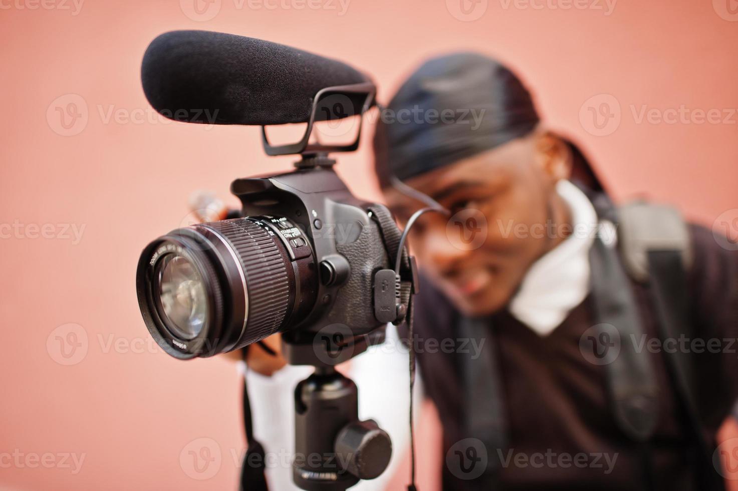 Young professional african american videographer holding professional camera with pro equipment. Afro cameraman wearing black duraq making a videos. photo