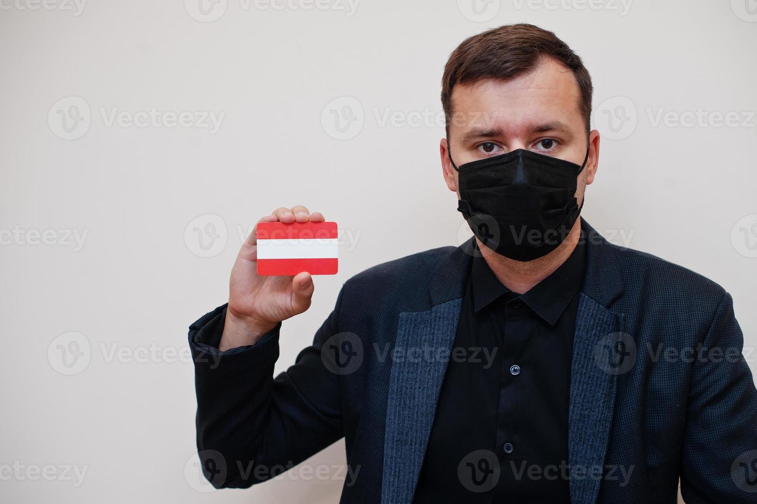 European man wear black formal and protect face mask, hold Austria flag card isolated on white background. Europe coronavirus Covid country concept. photo