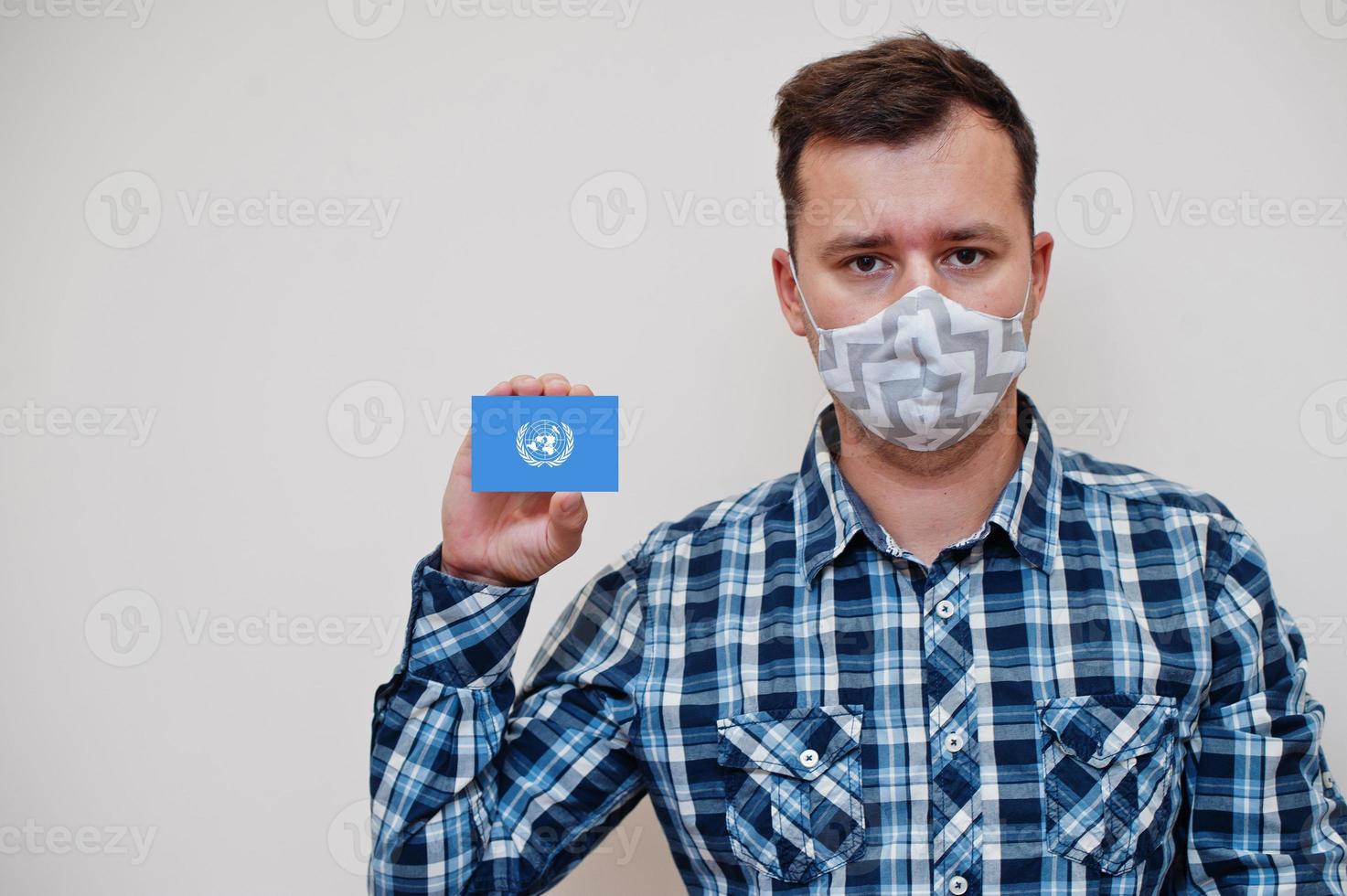 Man in checkered shirt show United Nations flag card in hand, wear protect mask isolated on white background. Europe countries Coronavirus concept. photo