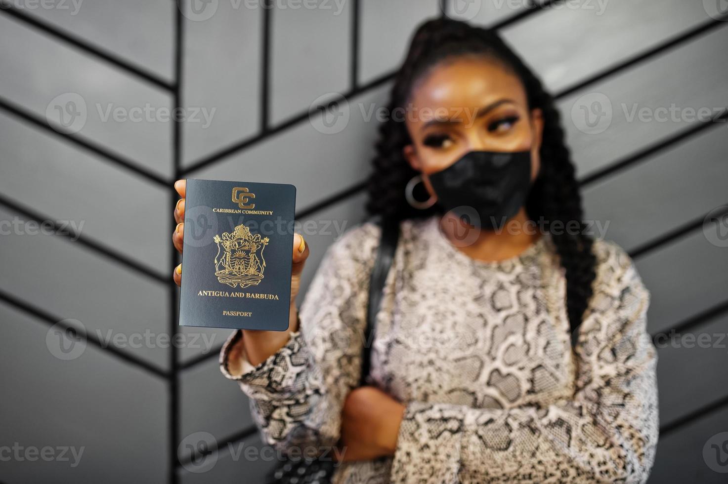 mujer afroamericana con mascarilla negra muestra el pasaporte de antigua y barbuda en la mano. coronavirus en el país de América, cierre de fronteras y cuarentena, concepto de brote de virus. foto