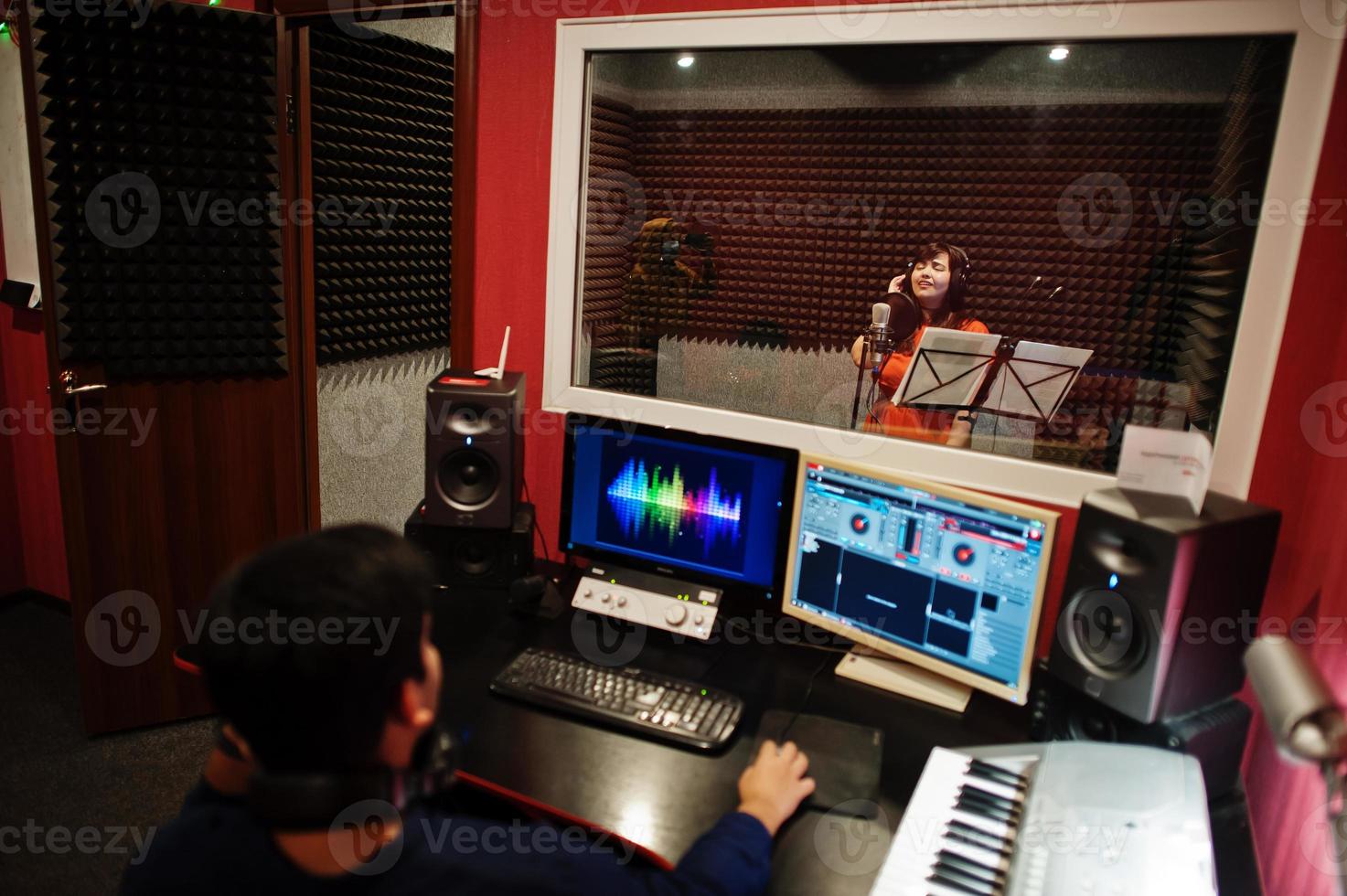 Young asian singer with microphone recording song in record music studio with sound producer. photo