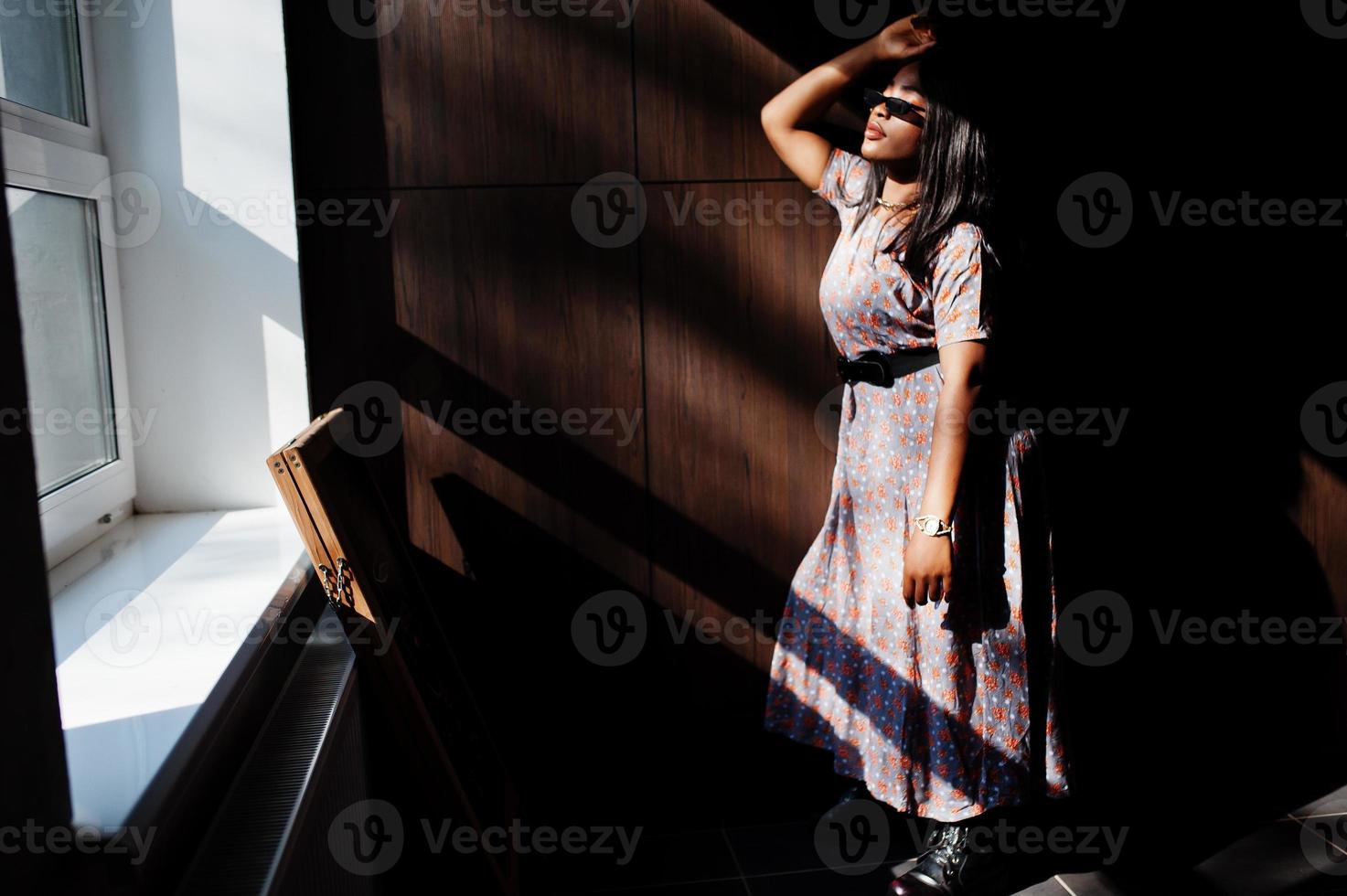 Game with shadows. Fashion portrait of african american woman in long dress and eyeglasses indoor. photo