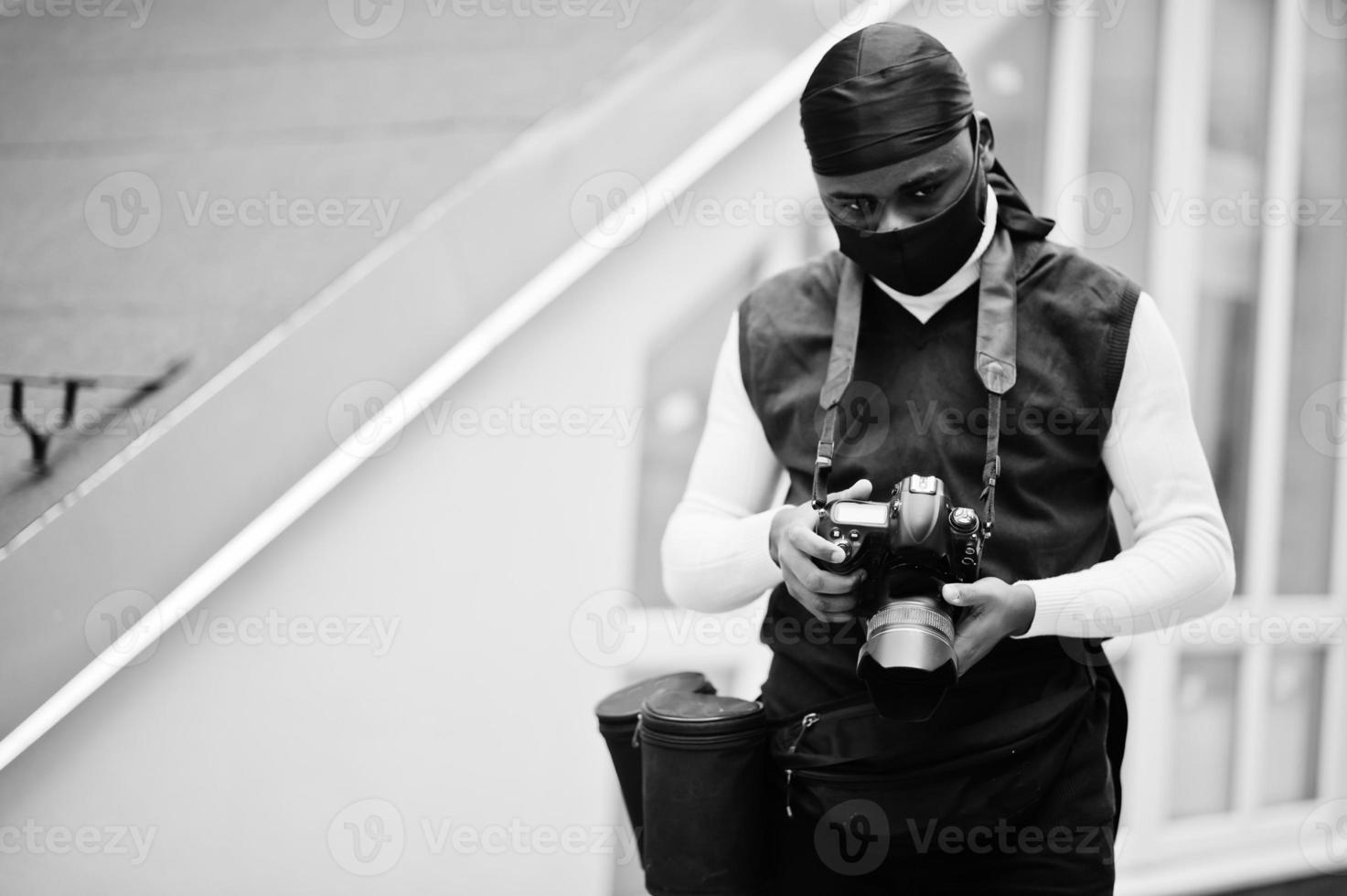 Young professional african american videographer holding professional camera with pro equipment. Afro cameraman wearing black duraq and face protect mask, making a videos. photo