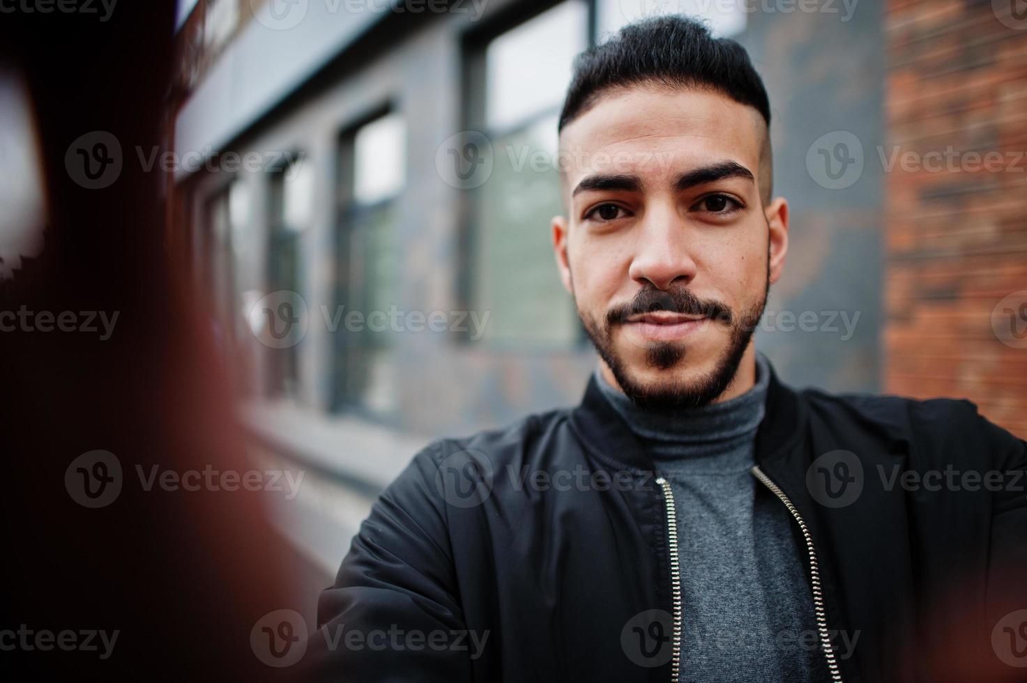 Portrait of stylish arab beard man wear grey turtleneck and black jaket. Arabian model guy make selfie by camera. photo