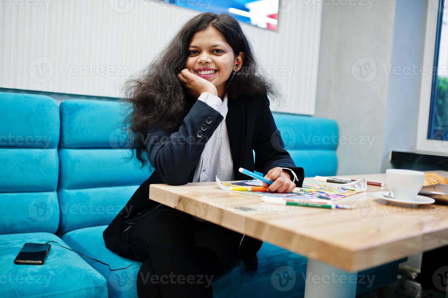 Indian artist woman wear formal paint picture and listening hindu music from earphones,while sitting at cafe. photo