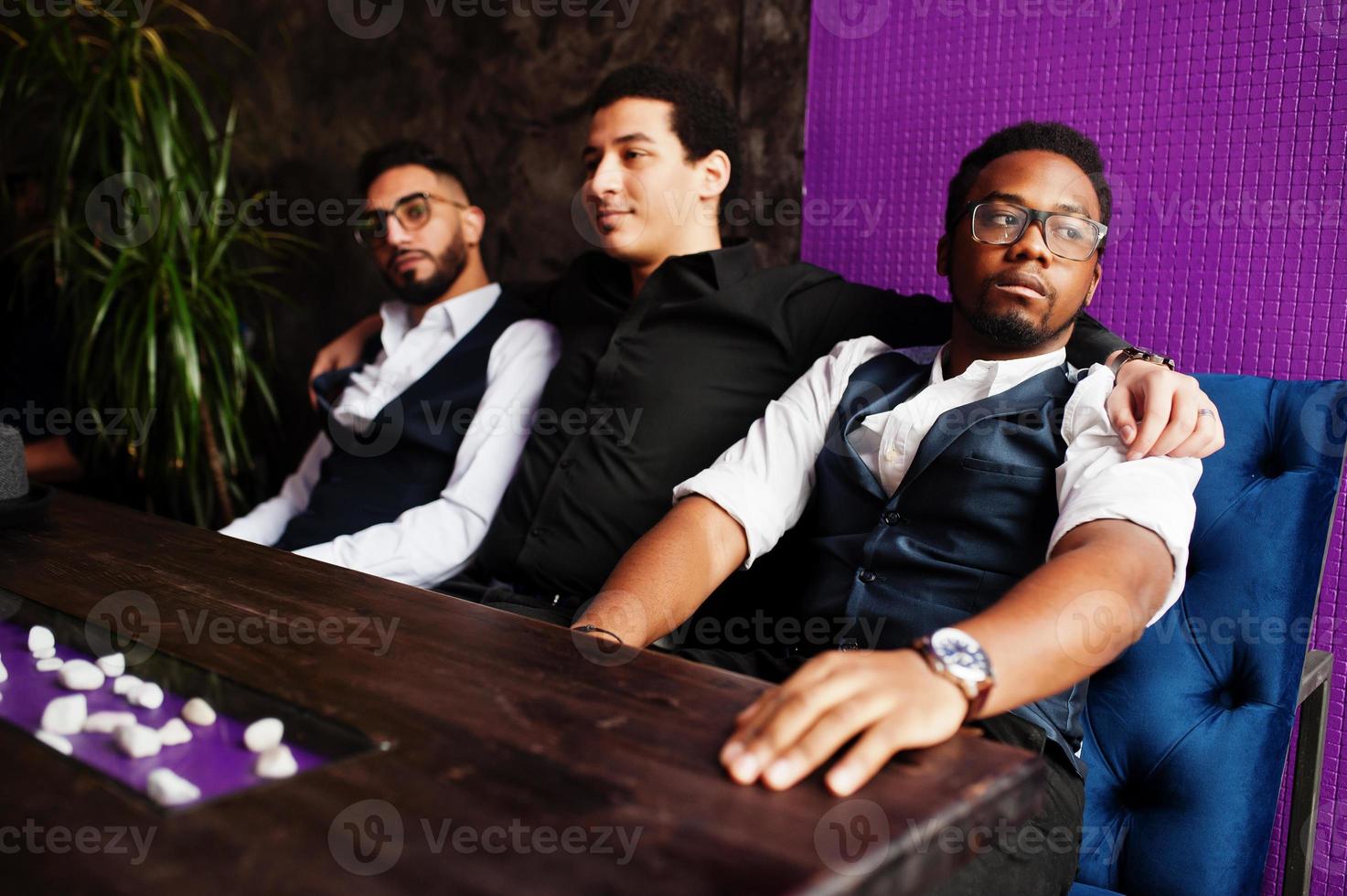 Group of handsome retro well-dressed man gangsters spend time at club. Multiethnic male bachelor mafia party in restaurant, sitting by table. photo