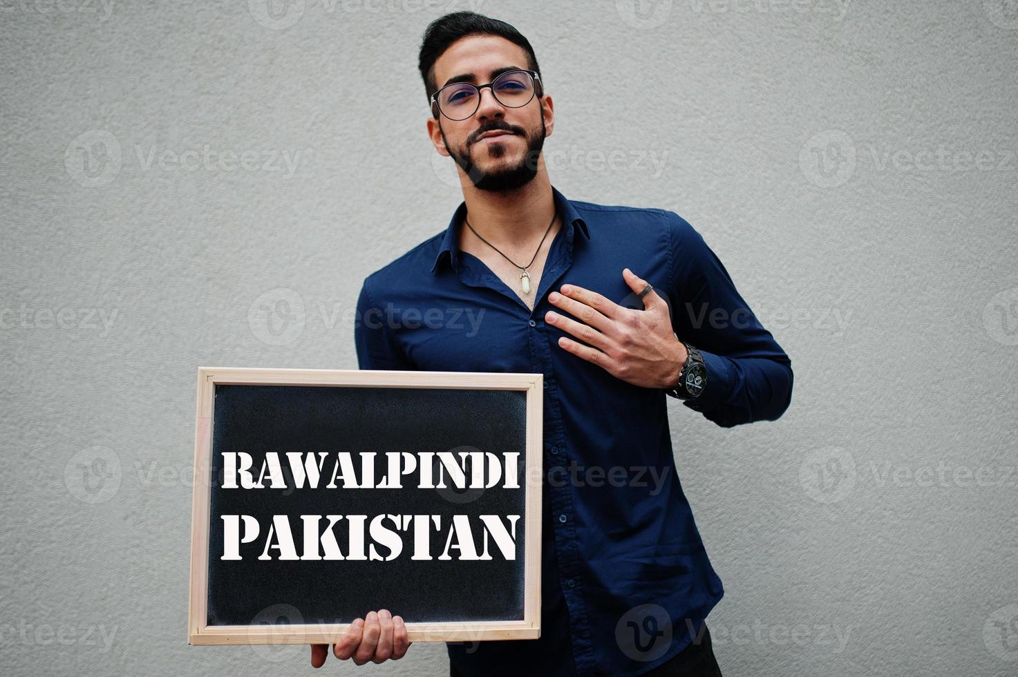 Arab man wear blue shirt and eyeglasses hold board with Rawalpindi Pakistan inscription. Largest cities in islamic world concept. photo