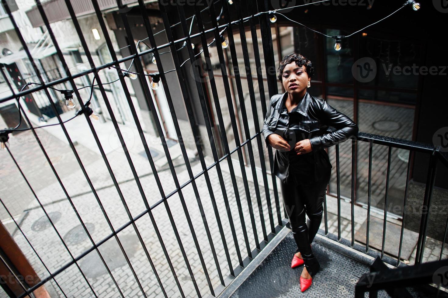 moda hermosa mujer afroamericana posando en chaqueta de cuero negro y pantalones en la calle. foto
