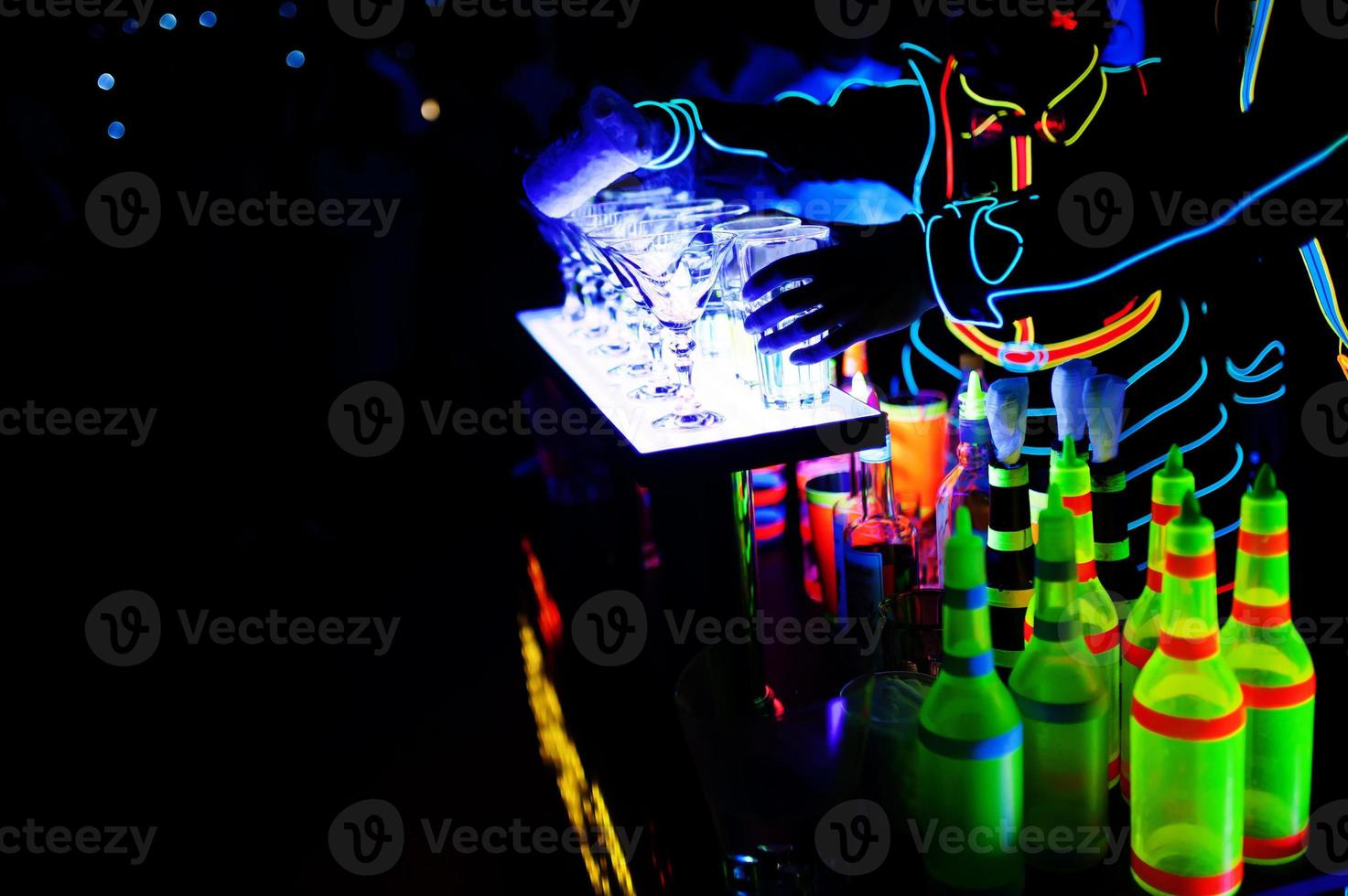 Professional barman and led light show. Silhouette of modern bartender shaking drink at night cocktail bar. photo