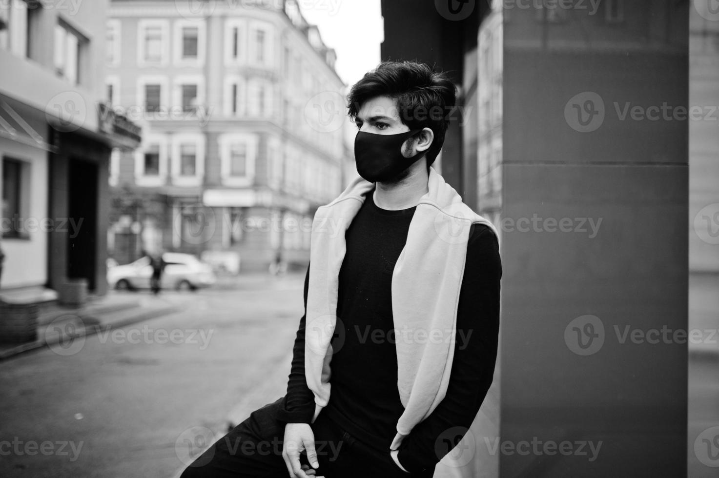 hombre indio joven hipster urbano en una sudadera amarilla de moda. un chico genial del sur de Asia usa una sudadera con capucha y una máscara de protección facial negra, durante la nueva normalidad. foto
