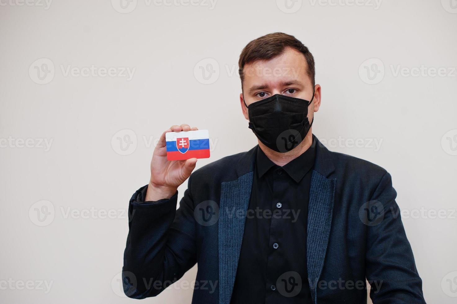 European man wear black formal and protect face mask, hold Slovakia flag card isolated on white background. Europe coronavirus Covid country concept. photo