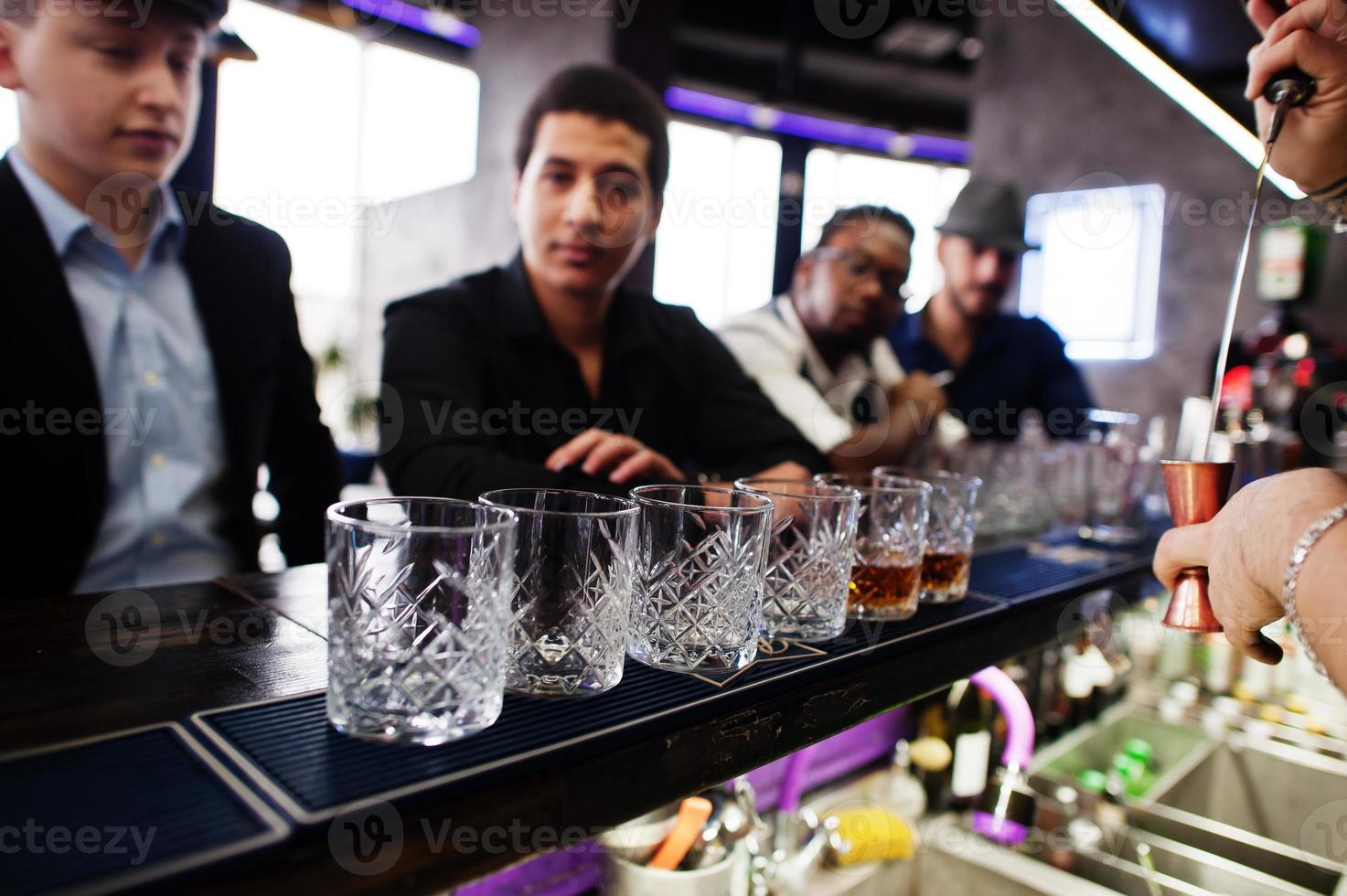 Group of handsome retro well-dressed man gangsters spend time at club. Drinking whiskey at bar counter. Multiethnic male bachelor mafia party in restaurant. photo