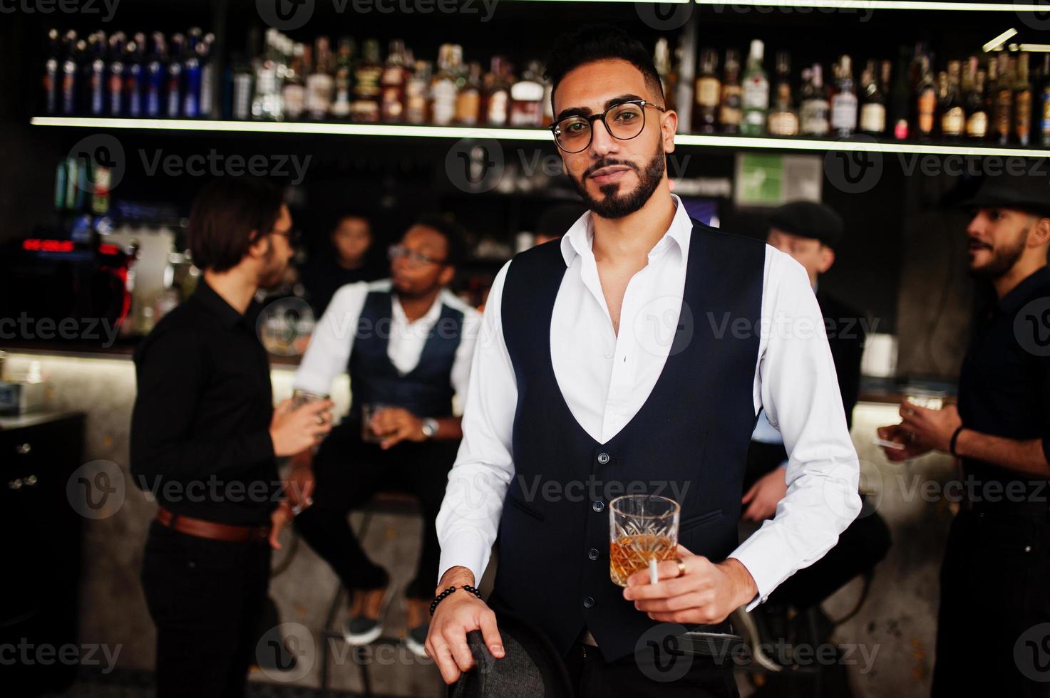 Stylish arab man against group of handsome retro well-dressed guys gangsters spend time at club, drinking on bar counter. Multiethnic male bachelor mafia party in restaurant. photo