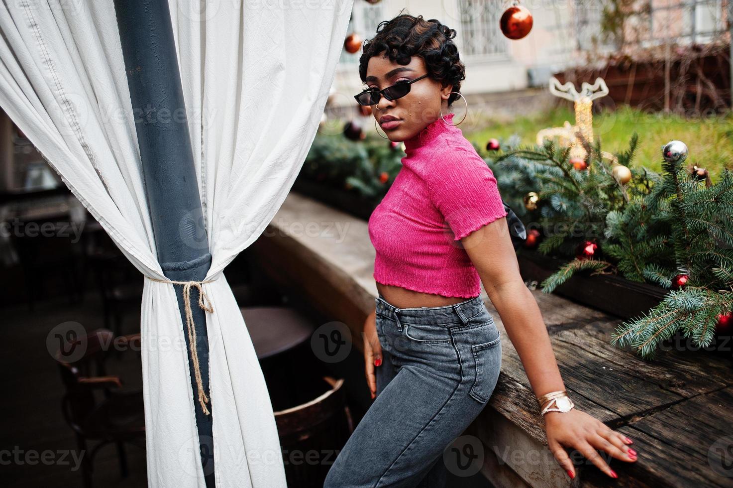 mujer afroamericana joven urbana en top rosa y jeans grises y gafas de sol con bolso. mujeres afro moda chic. foto