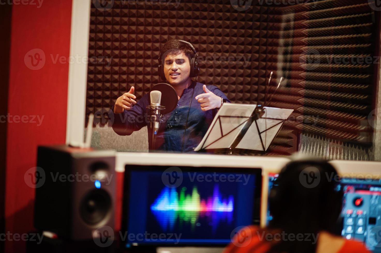 Young asian singer man with microphone recording song in record music studio with sound producer. photo