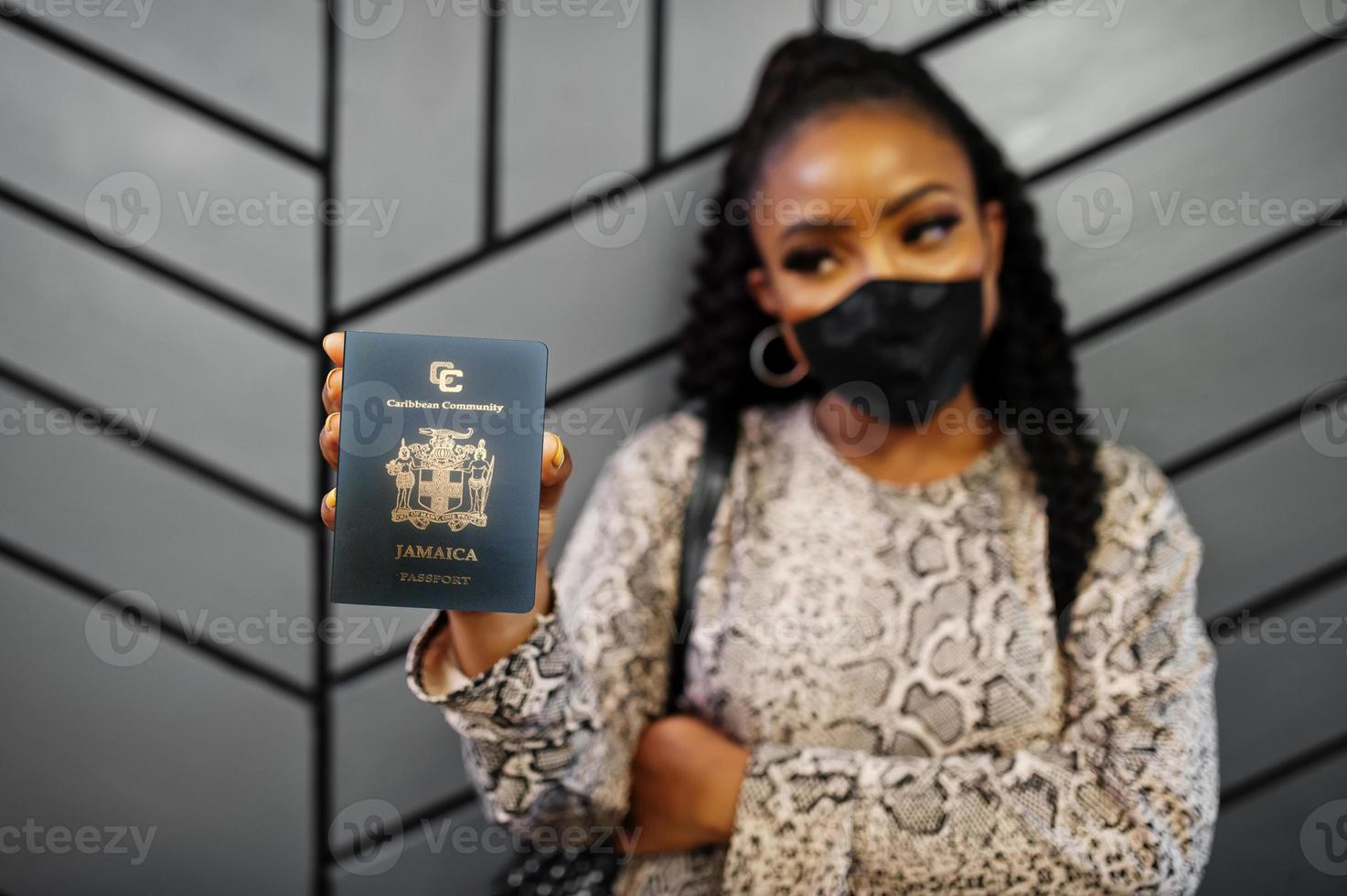 African american woman wearing black face mask show Jamaica passport in hand. Coronavirus in America country, border closure and quarantine, virus outbreak concept. photo