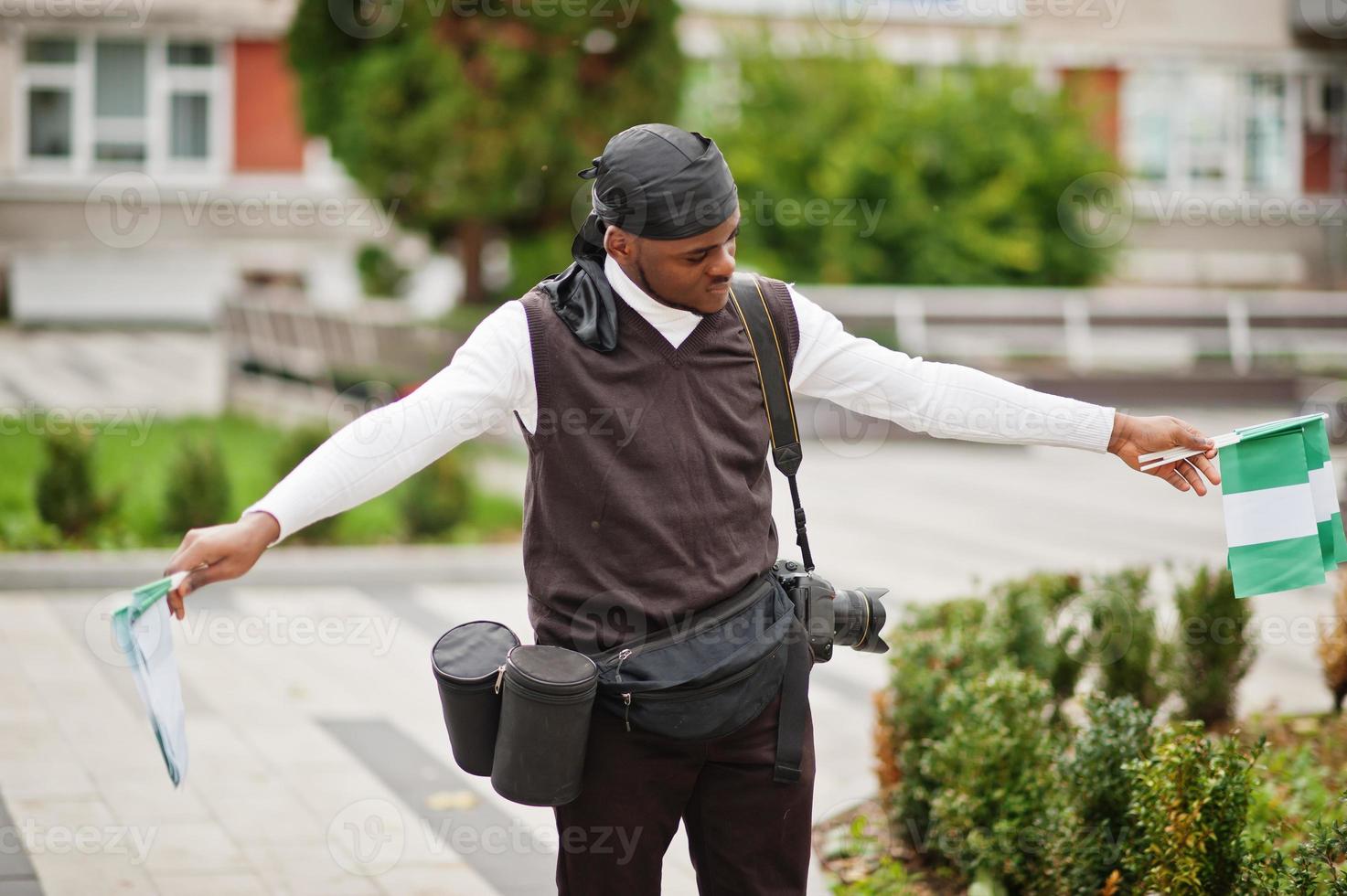 joven camarógrafo afroamericano profesional sosteniendo una cámara profesional con banderas nigerianas en las manos. foto