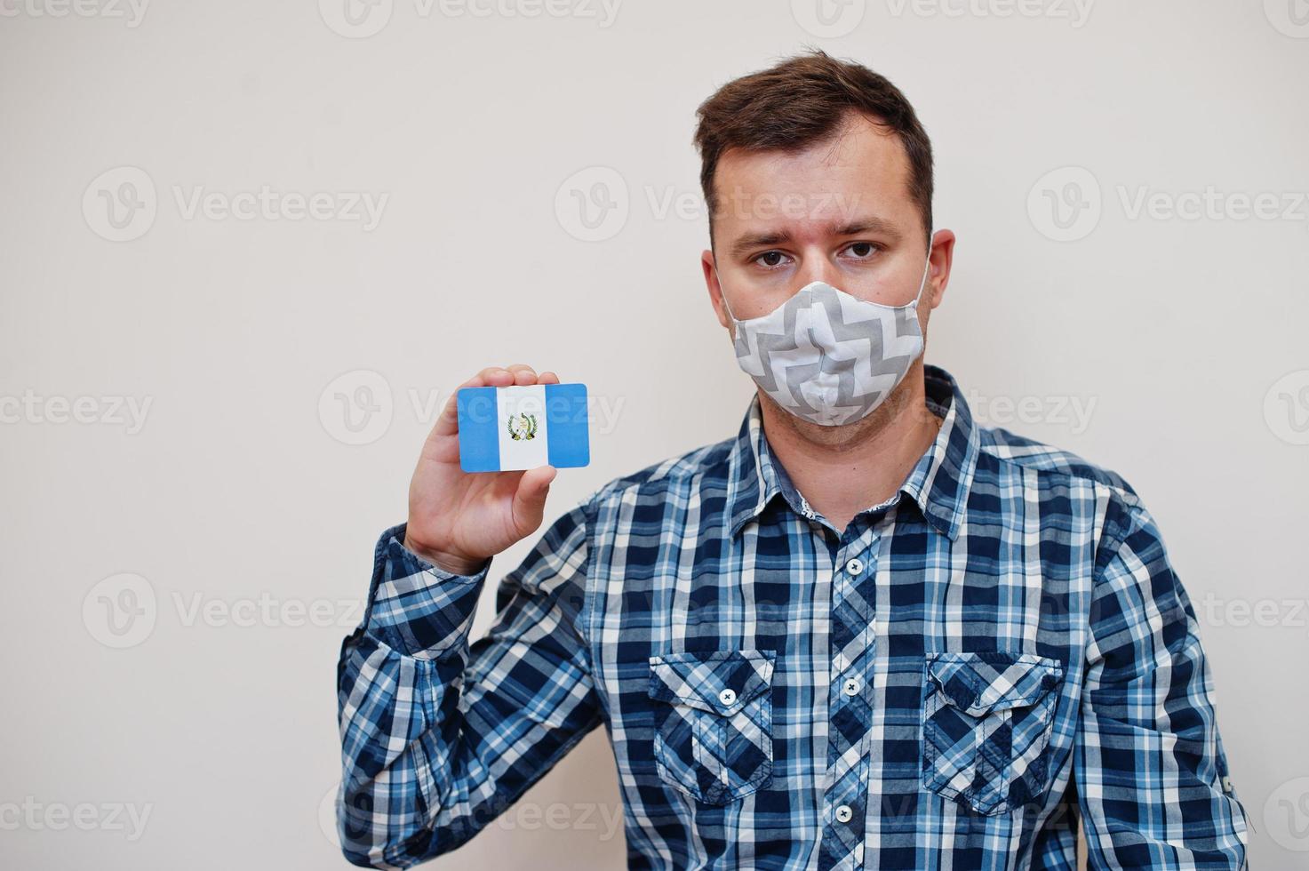 Man in checkered shirt show Guatemala flag card in hand, wear protect mask isolated on white background. American countries Coronavirus concept. photo