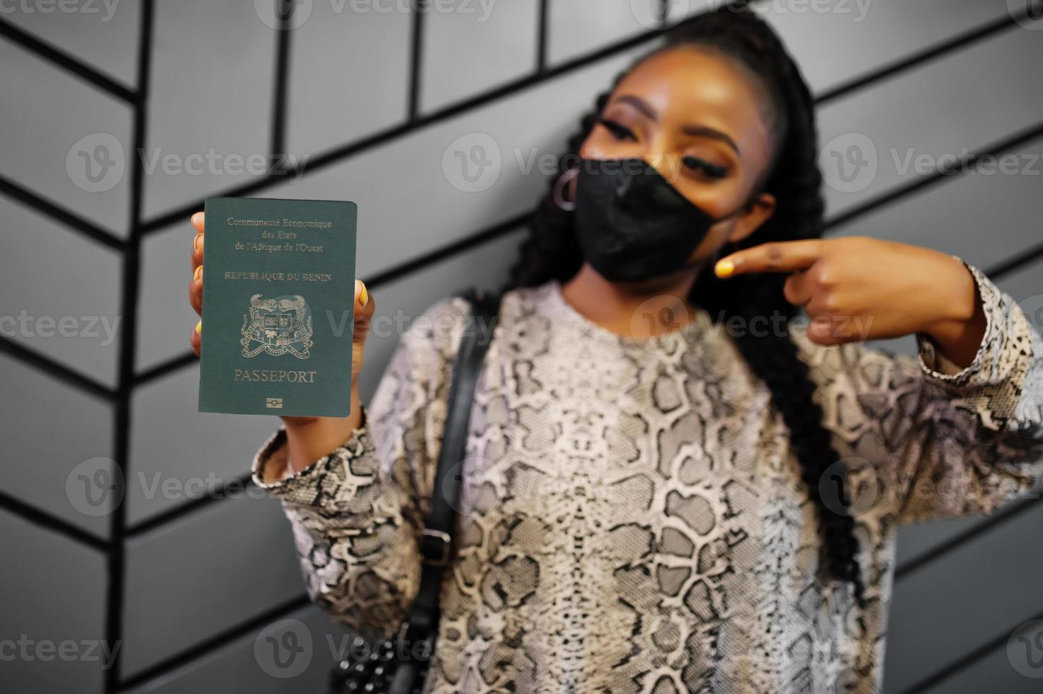 African woman wearing black face mask show Benin passport in hand. Coronavirus in Africa country, border closure and quarantine, virus outbreak concept. photo