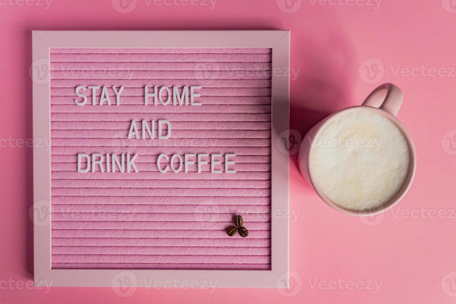 Top view of Pink Coffee cup with cappuccino and qoute Stay home and drink coffee. Self isolation and quarantine campaign to protect yourself from pandemia. photo