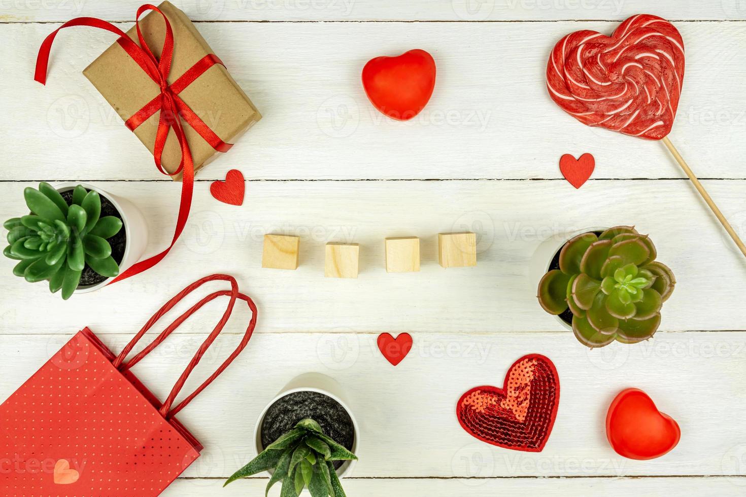 Creative Valentine Day romantic composition with red hearts, satin ribbon, lollipop, gift box and paper bag on white background. Mockup with empty wooden cubes for text. photo