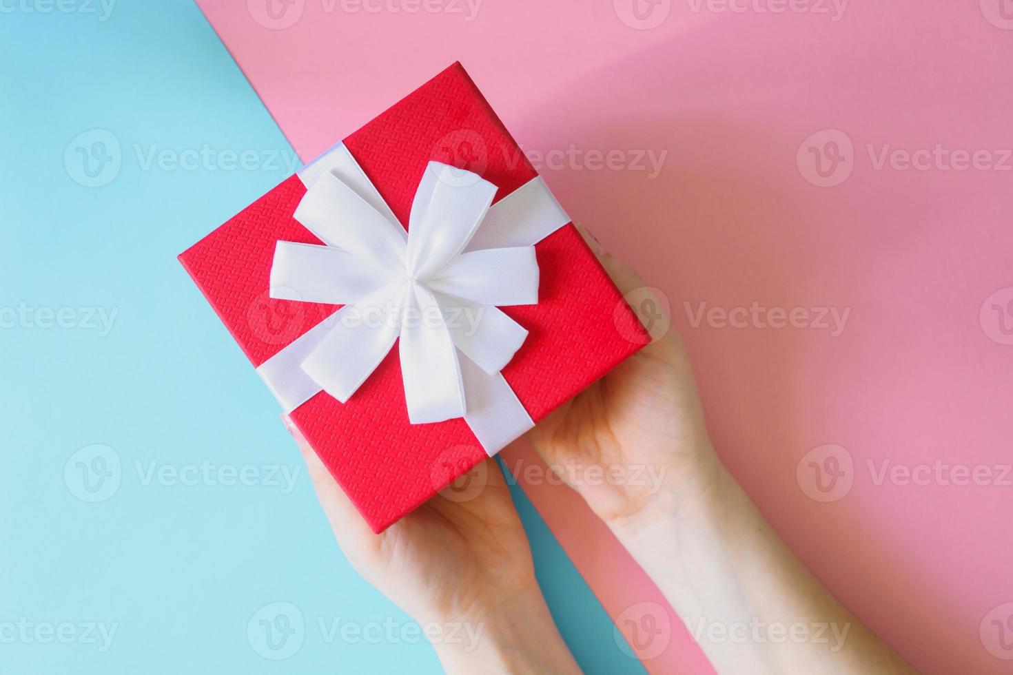 Woman holding red gift box on color blue and pink background. Festive greeting card. Holiday concept photo