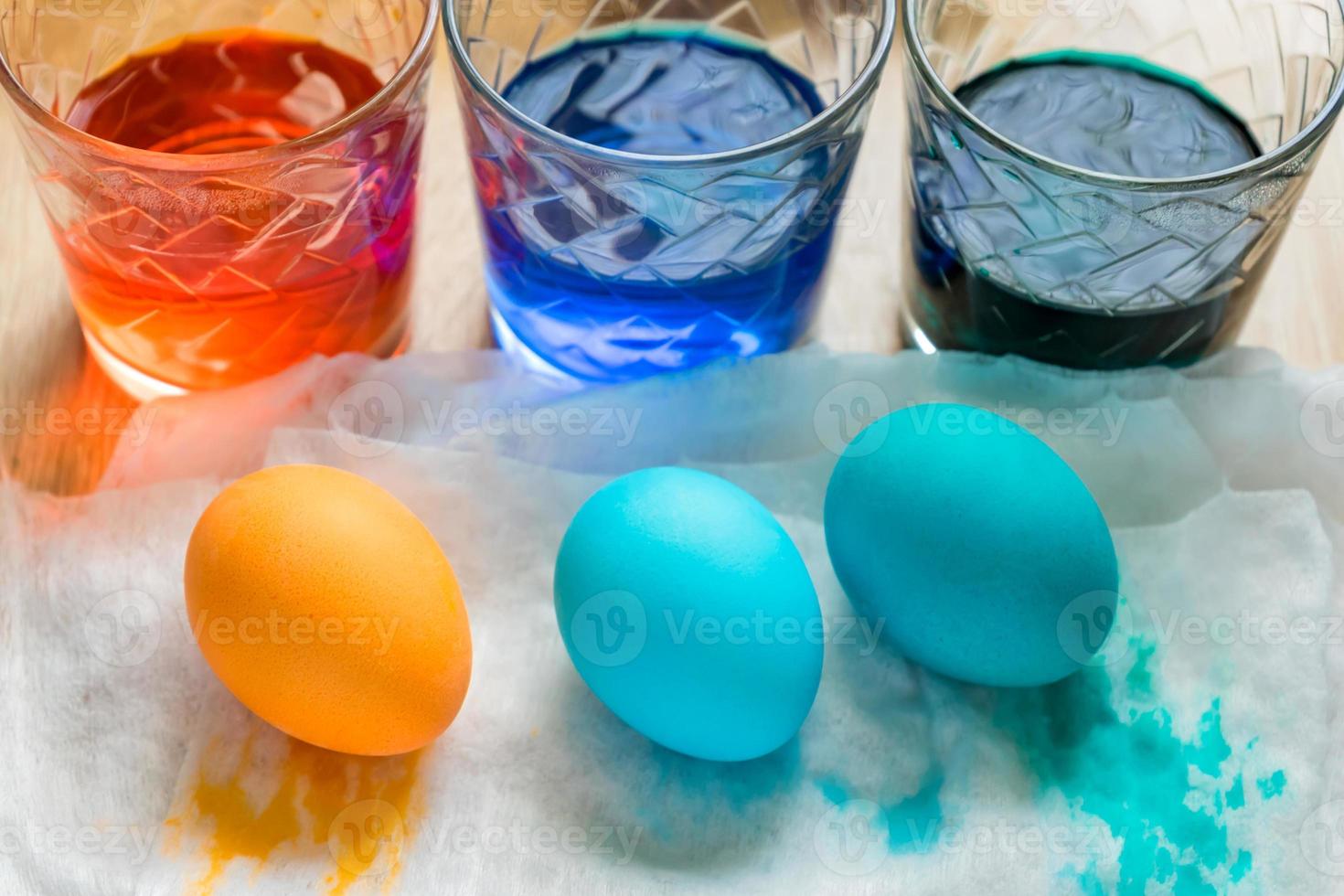 proceso de muerte del huevo de pascua. vasos de vidrio transparente con agua coloreada y huevos coloreados, vista superior foto